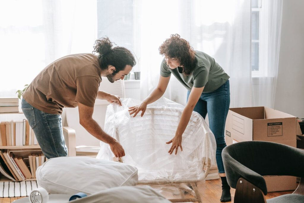 Two people wrapping furniture 
